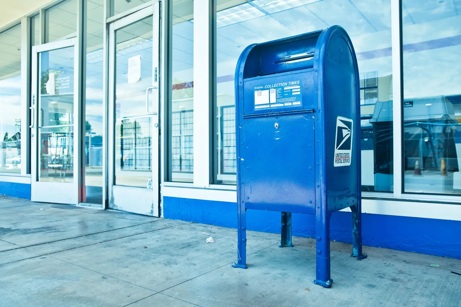 USPS blue mailbox against a post office facade in Los Angeles, CA. How USPS mailing rules decide which imprint machinery a US print shop buys